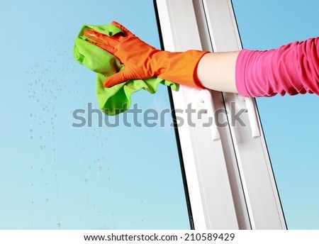 hand in orange glove cleaning window with green rag