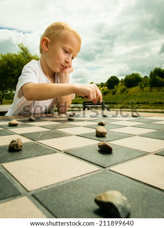 Draughts board game. Little boy clever child kid playing checkers thinking, outdoor in the park. Childhood and development