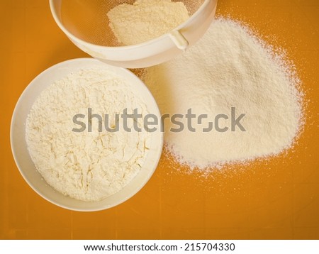 Cooking concept. Preparation for baking, bake ingredients and kitchen tools to make a cake, sifting wheat flour on orange nonstick silicone mat, top view