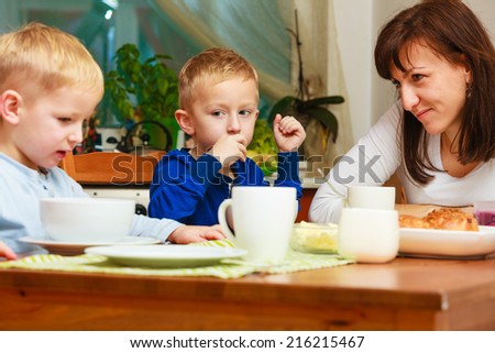 Happy family. Mother and sons boys kids children eating corn flakes and bread breakfast morning meal together at the table. Home.