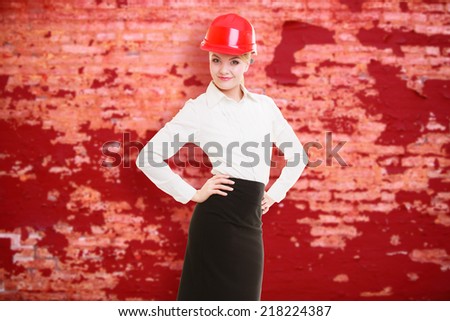 Portrait of attractive female engineer. Woman architect in red safety helmet on old brick wall background with blank copy space. Building.