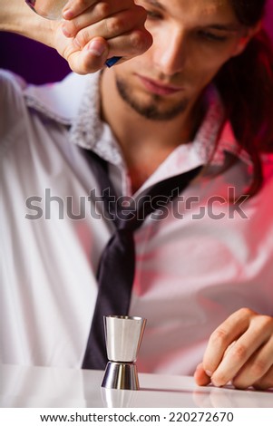 Young stylish man bartender preparing serving alcohol cocktail drink, pouring vodka filling a jigger