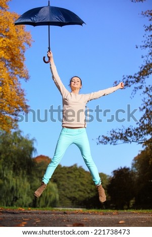 Happiness and freedom. Casual young woman girl jumping with blue umbrella in autumnal park, having fun outdoor