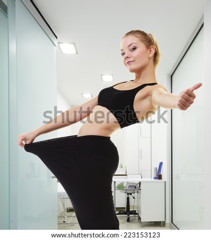 Weight loss and healthy lifestyle. Happy woman fitness girl showing how much weight she lost, giving thumb up success hand sign in clinic interior