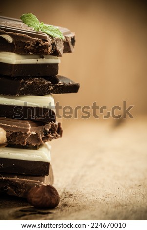 Closeup stack of different sorts chocolate pieces and hazelnut. Variety of chocolates on wooden table.