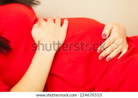 Pregnancy, motherhood and happiness concept. elegant pregnant woman in red dress relaxing on sofa and touching her belly. Part of body