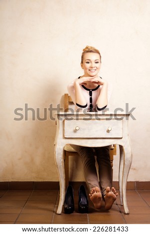 Vintage style. Full length of barefoot girl student or businesswoman sitting on the wooden chair at the white retro desk. Design.