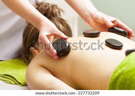 Day-spa. Young woman in green towel relaxing in healthy spa salon. Girl having hot stone massage. Indoor.