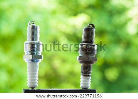 Auto service. Two car spark plugs new and old as spare part of auto transportation on blurry green background.
