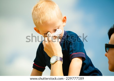 Child playing outdoor and blowing nose in handkerchief. Little boy kid sneezing in tissue. Catarrh or allergy to pollen symptom.