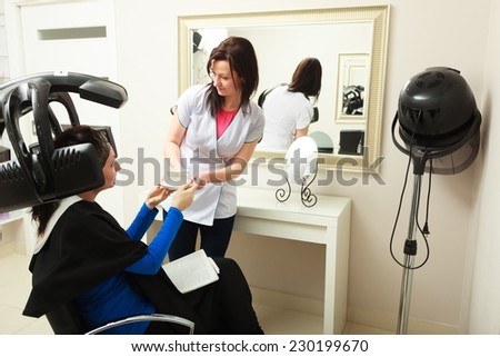 Hairdressing beauty salon. Hairdresser hairstylist giving cup of coffee tea hot beverage to female client. Young woman relaxing in hair salon. Modern equipment.
