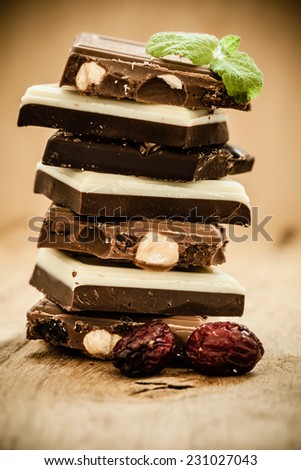 Closeup stack of different sorts chocolate pieces and cranberry. Variety of chocolates on wooden table.