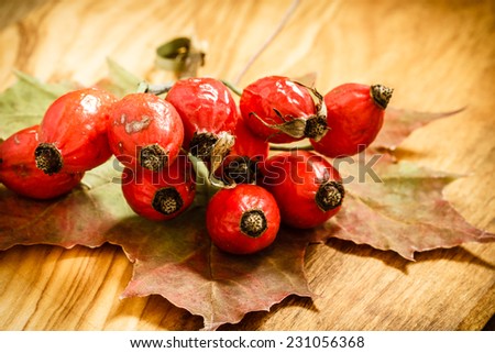 Hawthorn and maple leaf on wooden rustic table background. Rose hips haw fruit of the dog rose.