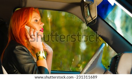Concept of danger driving. Young woman driver redhaired girl talking on mobile phone smartphone while driving the car.
