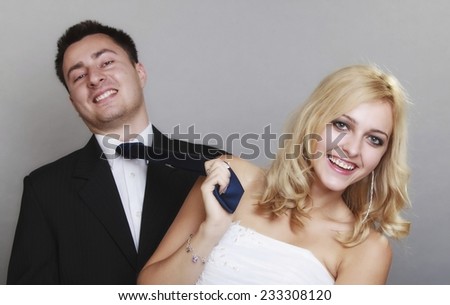 Wedding day. Portrait of happy married couple blonde bride and groom. Woman pulling on mans tie, studio shot on gray background
