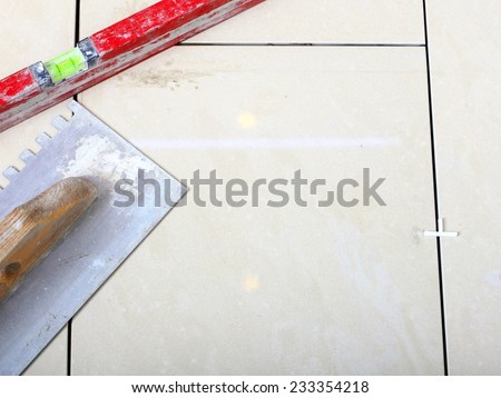 construction equipment dirty notched trowel and level on new tile floor surface, tile floor adhesive