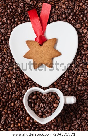 Christmas time concept. Gingerbread cookie star shaped on saucer, white cup in shape of heart on coffee beans background