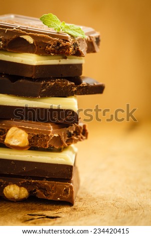 Closeup stack of different sorts chocolate pieces. Variety of chocolates on wooden table.