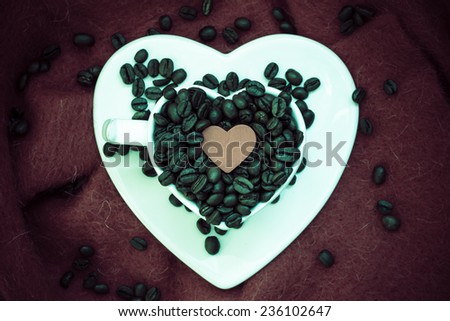 Coffee klatsch java concept. Heart shaped white cup filled with roasted coffee beans on brown cloth background