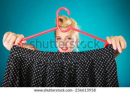 Pinup girl young woman in retro style buying clothes. Client holding black skirt on vibrant blue. Retail and sale. Studio shot.