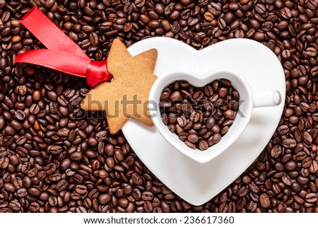 Christmas time concept. Gingerbread cookie star shaped, white cup with saucer in shape of heart on coffee beans background
