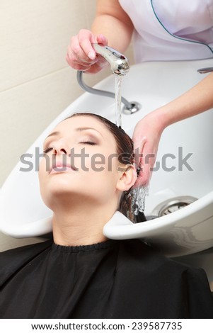 Hairstylist hairdresser washing customer hair. Brunette girl young woman relaxing in hairdressing beauty salon.
