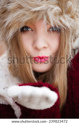 Winter fashion. Closeup young woman wearing fashionable wintertime clothes fur cap blowing a kiss outdoor portrait