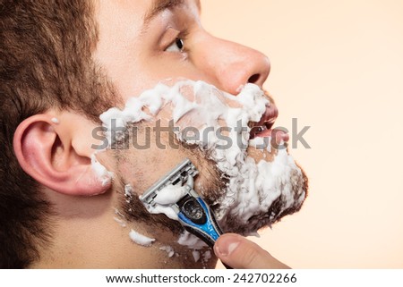 Health beauty and skin care concept. Closeup young bearded man with foam on face shaving on bright orange background.