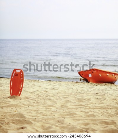 Beach life-saving. Lifeguard rescue equipment orange preserver tool and boat, red plastic buoyancy aid in the sand