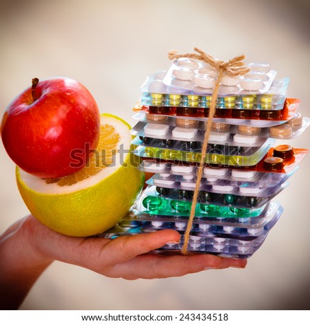 Health and balanced diet concept. Choice between two sources of vitamins - pills or fruits. Closeup female hand holding stack of drugs apple and grapefruit