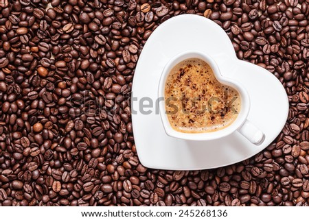 Hot beverage. White coffee cup heart shaped with cappucino latte on roasted beans background