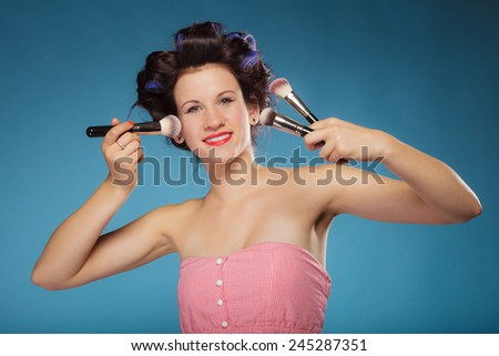 Cosmetic beauty procedures and makeover concept. Woman in hair rollers holding makeup brushes set on blue