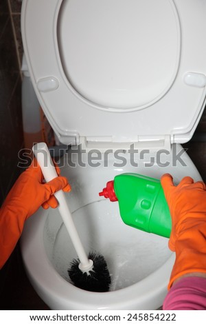 Female hand in orange rubber glove cleaning toilet bowl using brush. Clean up your house.