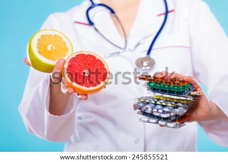 Health and balanced diet concept. Choice between two sources of vitamins - pills or fruits. Medical doctor offering chemical and natural vitamins, holding stack of drugs and grapefruits on blue.