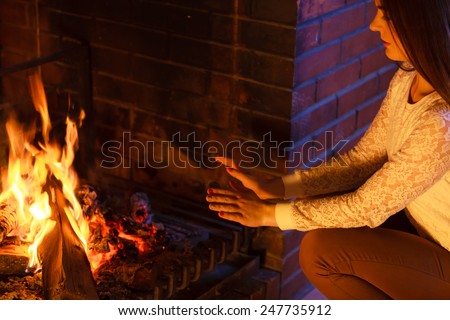 Winter at home. Young woman beauty long hair girl warming her hands at fire fireplace interior. Heating.