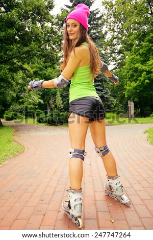 Happy young girl enjoying roller skating rollerblading on inline skates sport in park. Woman in outdoor activities