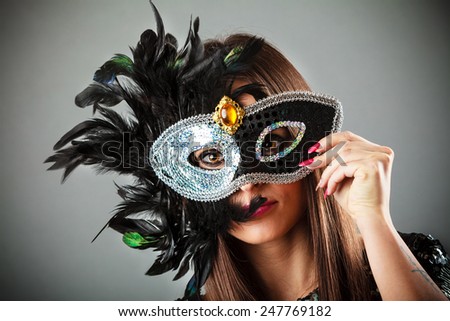 Carnival night life. Attractive woman face with hand holding mysterious mask on grey background in studio.