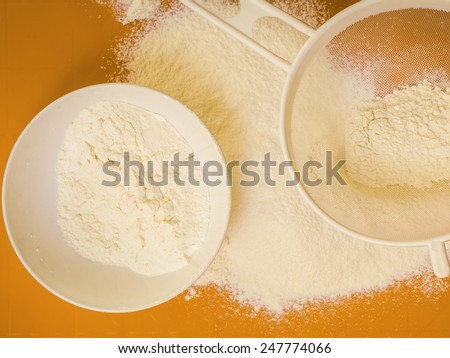 Cooking concept. Preparation for baking, bake ingredients and kitchen tools to make a cake, sifting wheat flour on orange nonstick silicone mat, top view