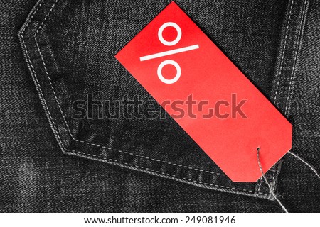 Shopping and sale concept. Closeup red label with percent sign and copy space on black jeans pocket denim cotton material background