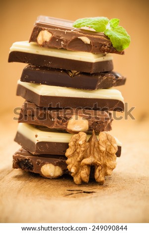 Closeup stack of different sorts chocolate pieces and walnut. Variety of chocolates on wooden table.