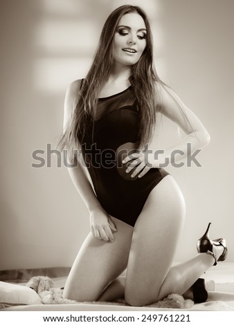 Full length beautiful alluring young woman in black lingerie with long hair posing on bed in retro vintage high heels shoes, aged black ehite tone