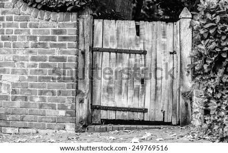 Countryside scene. Rustic old wooden gate in brick wall. Black and white photo