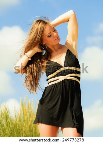 Vacation day on beach. Smiling happy standing woman black dress on sand.