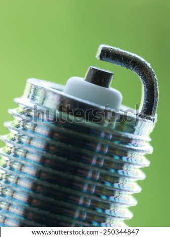 Auto service. New car spark plug as spare part of auto transportation on blurry green background.