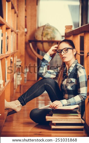 Education school concept. Clever female student hair ponytail girl glasses sitting on floor in college library with stack books. Indoor