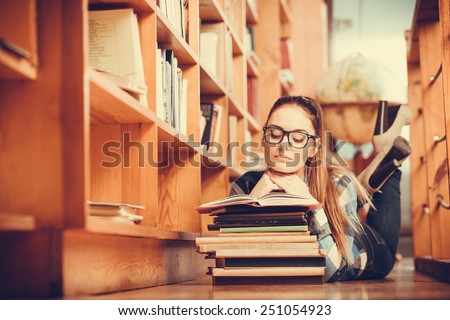 Education school concept. Clever female student girl in glasses lying on floor in college library with stack books reading. Instagram tone