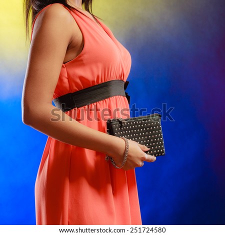 Fashion elegant evening outfit. Female hand holding black rivet leather handbag clutch bag on blue background