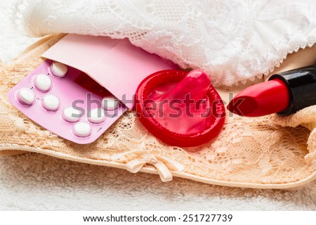 Healthcare medicine, contraception and birth control. Closeup oral contraceptive pills, condom and red lipstick on lace lingerie.