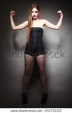 Full length of sad young woman with long hair and creative makeup. Unhappy girl showing her muscles power in dark. Negative emotions. Studio shot.