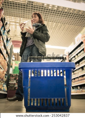 Woman shopping with blue basket at supermarket self-service grocery shop. Retail. Real.